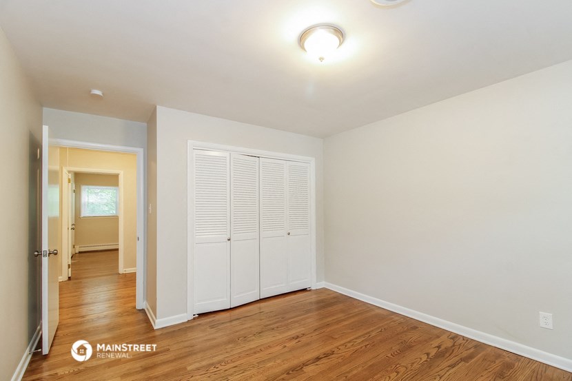 a living room with white walls and wood floors and a door to a hallway