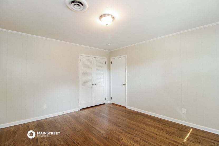 a bedroom with white walls and wood flooring and white closets