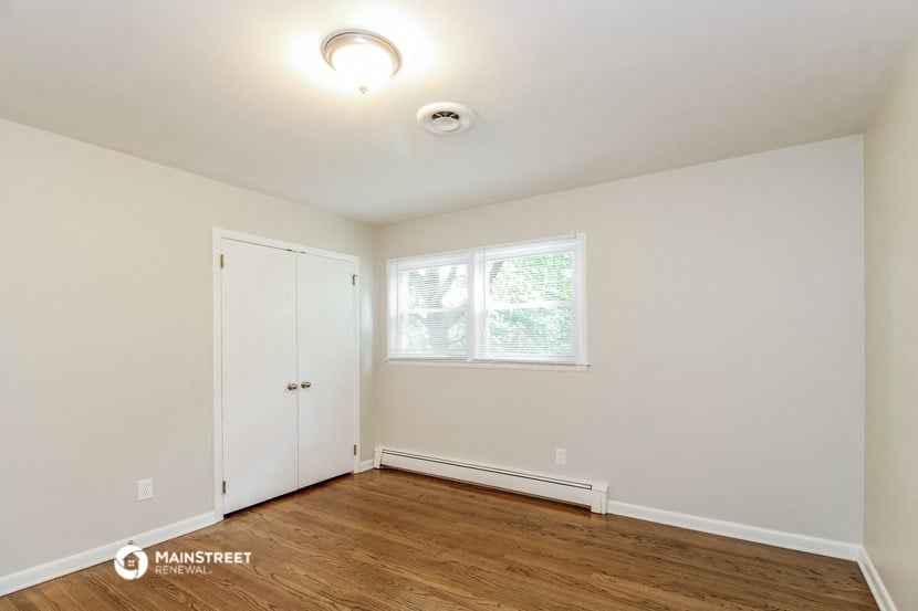 a bedroom with white walls and wood floors and a window