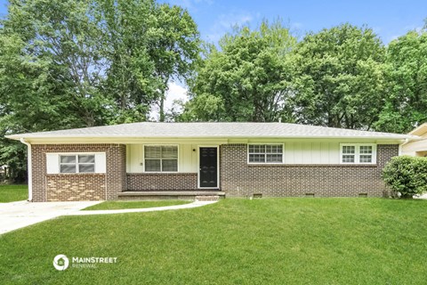 the front of a brick house with green grass and trees