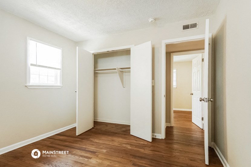 a bedroom with white walls and wood floors and an open closet