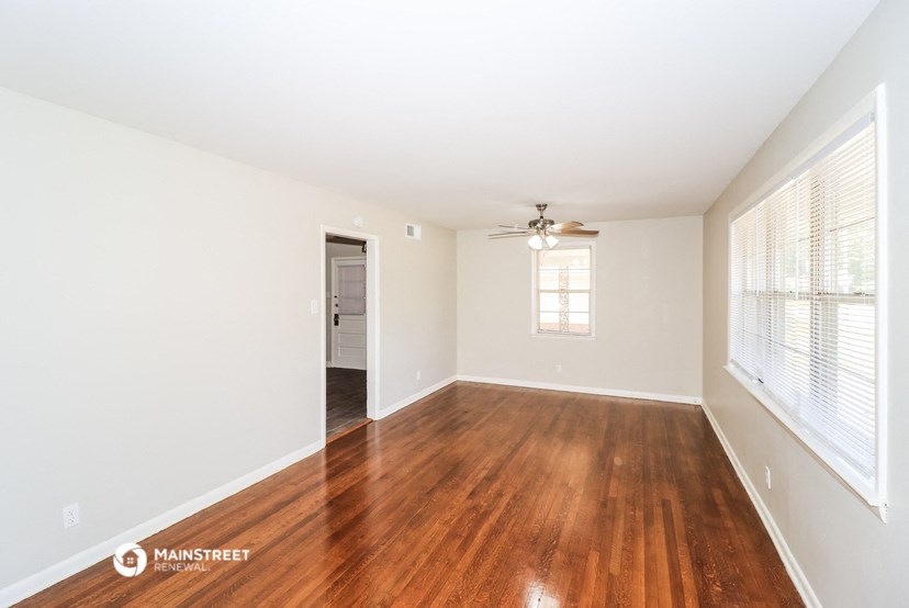 the spacious living room with wood flooring and a ceiling fan
