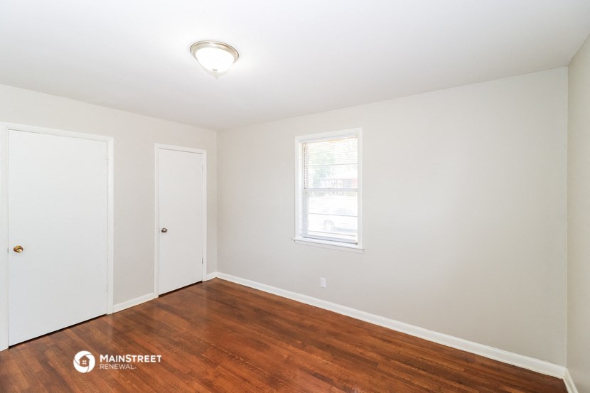 a bedroom with wood flooring and white walls and a window