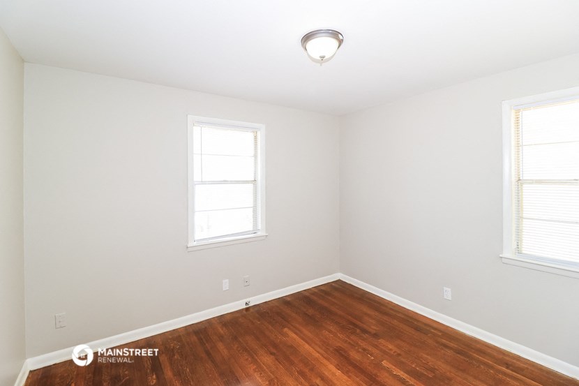 a bedroom with a hard wood floor and two windows