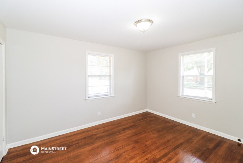 a bedroom with a hard wood floor and two windows