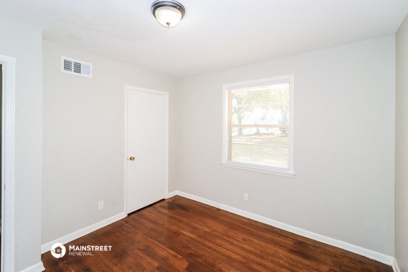 a bedroom with wood flooring and white walls and a window
