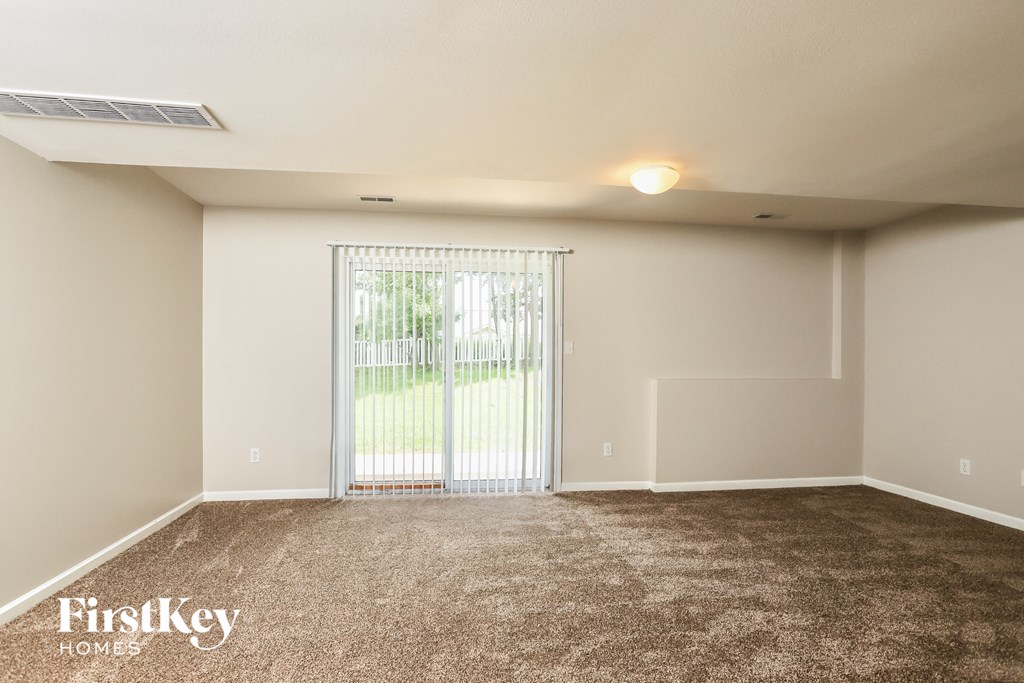 A room with a carpeted floor and a sliding glass door leading to a backyard.