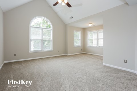 A spacious room with a ceiling fan and two windows.