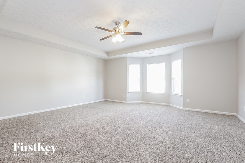 A spacious room with a carpeted floor and a ceiling fan.