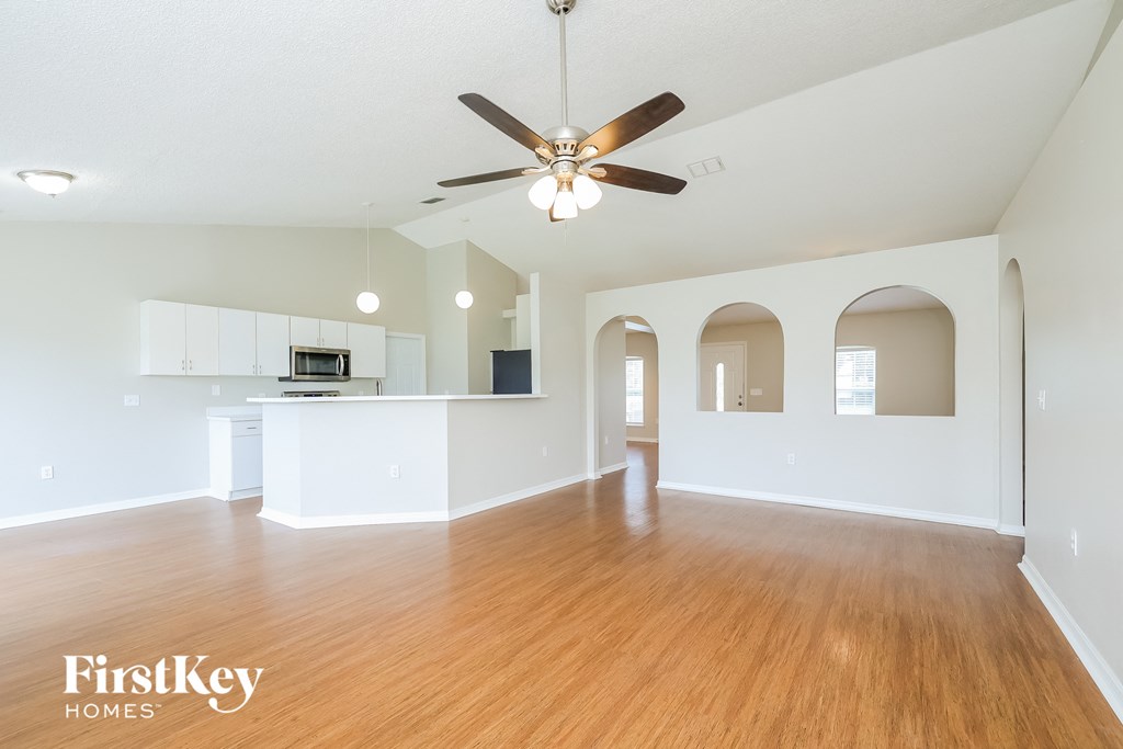 an empty living room with a ceiling fan and a kitchen