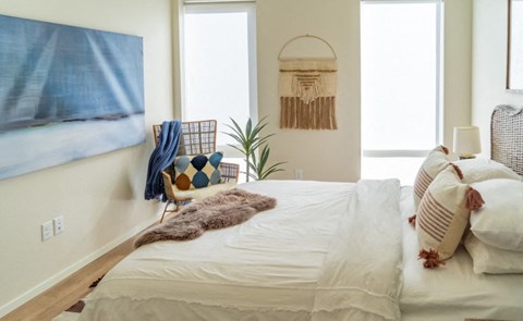 A bedroom with a bed, a chair, a plant, and a wall hanging.