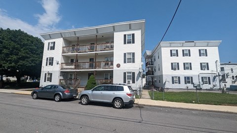 Two cars are parked in front of a white apartment building.