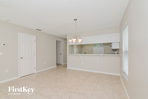 A spacious room with a chandelier and a kitchen area in the background.