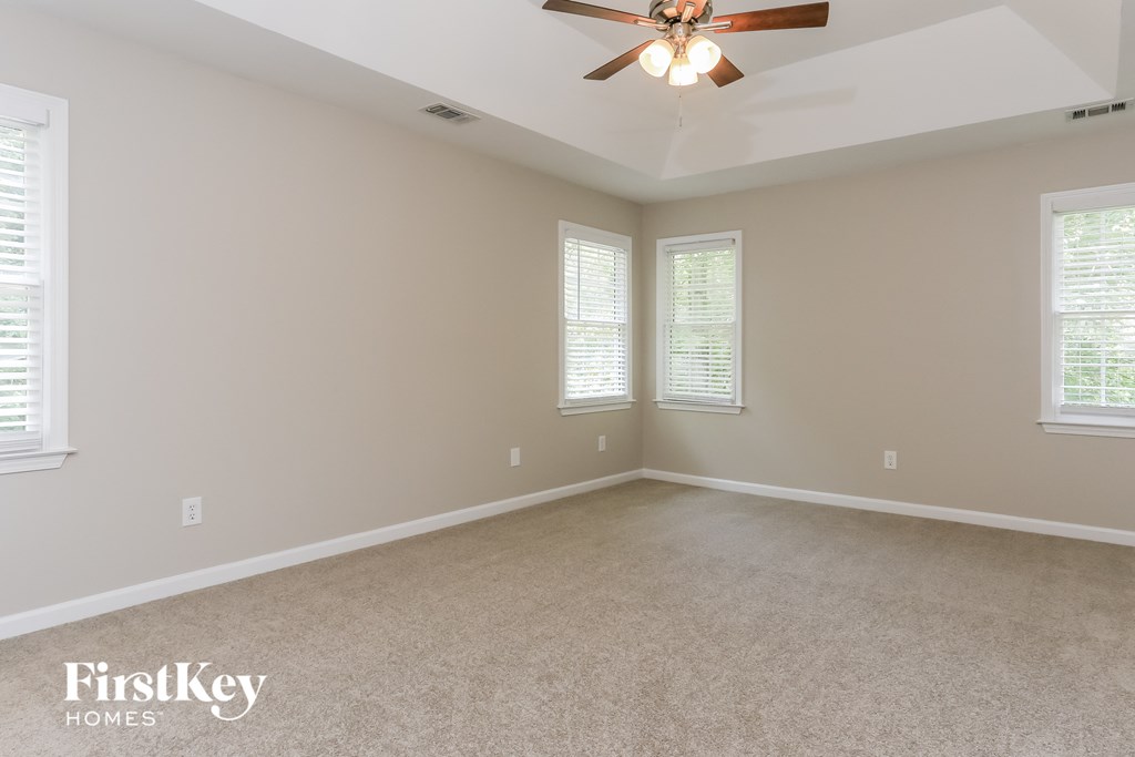 A spacious room with a ceiling fan and two windows.
