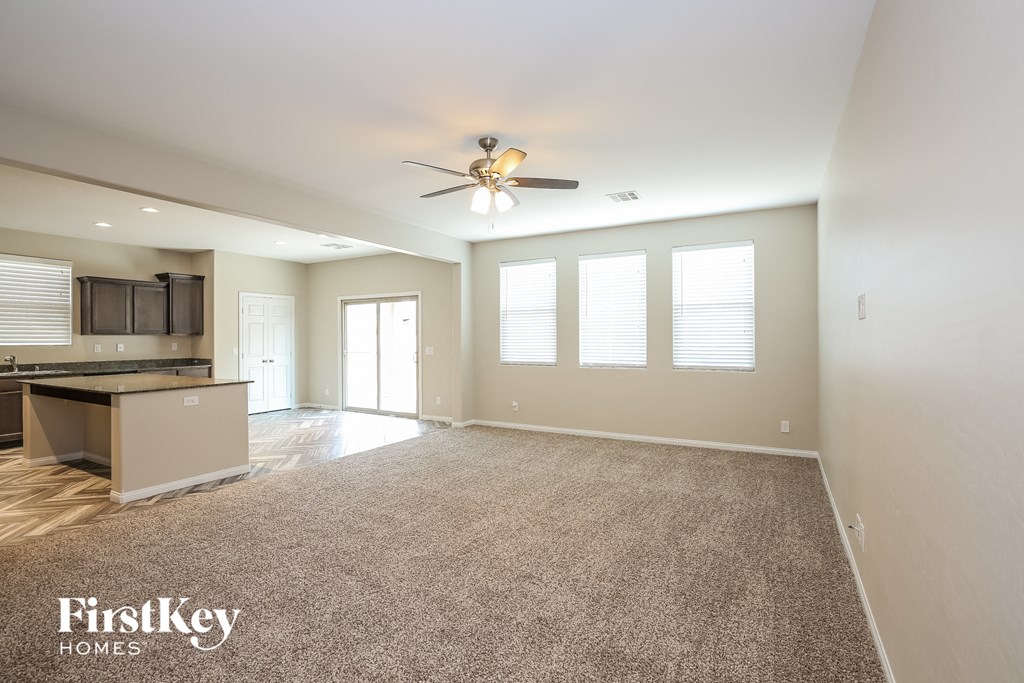 A spacious living room with a ceiling fan and carpeted floor.