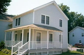 A white house with a porch and a car parked in the driveway.