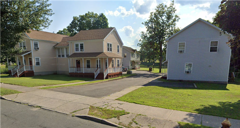 A white house is situated on the right side of a street.