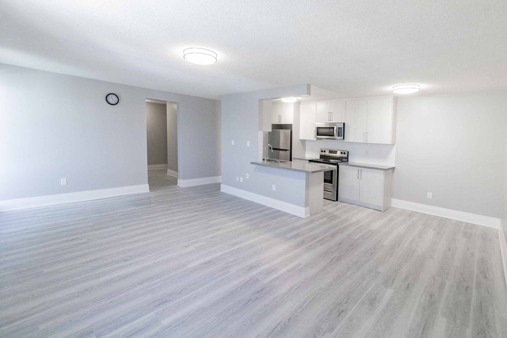 an empty living room with a kitchen with a stove and refrigerator