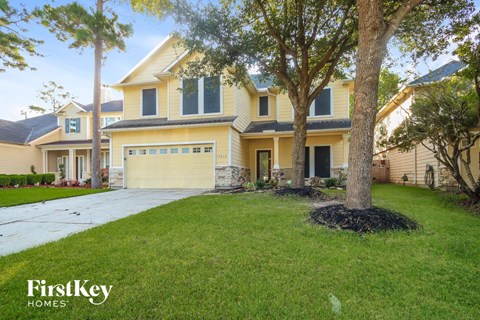 a large yellow house with a driveway and a tree