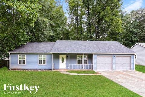 A blue house with a garage is surrounded by green trees.