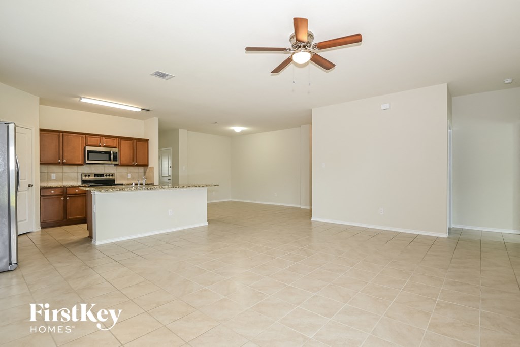 A spacious kitchen and living room with a ceiling fan and tiled flooring.