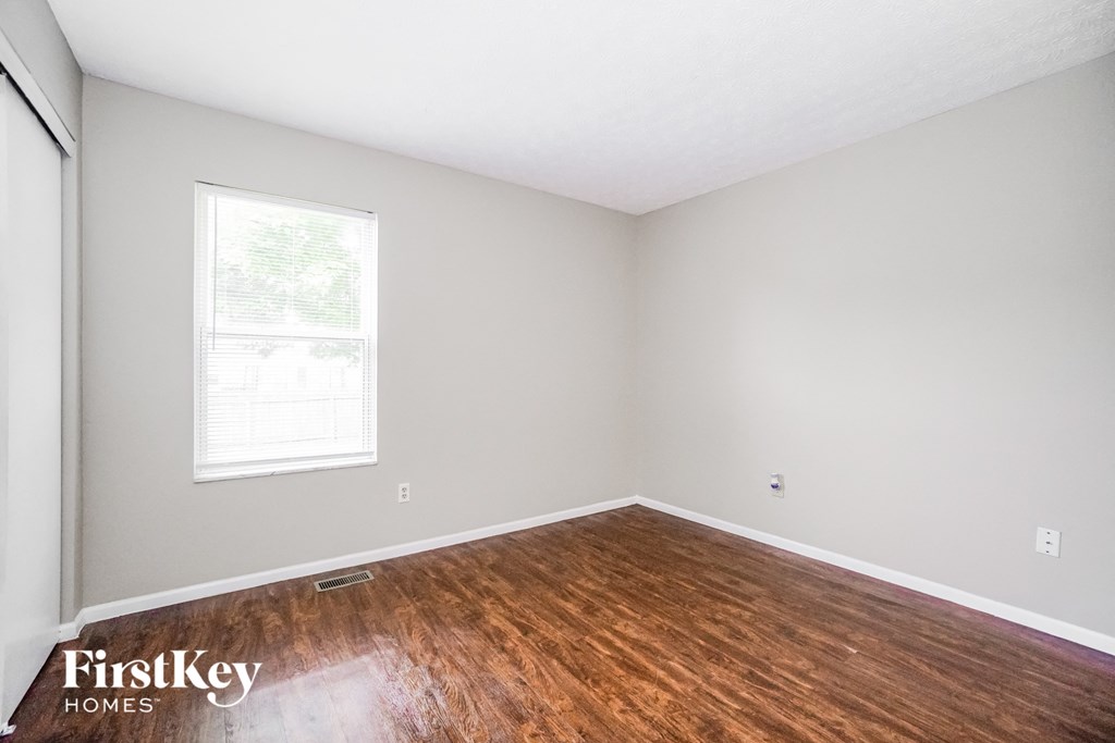 a bedroom with wood floors and white walls and a window
