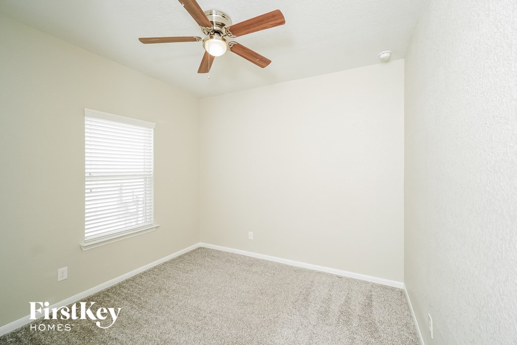 the spacious bedroom has a ceiling fan and carpeted flooring