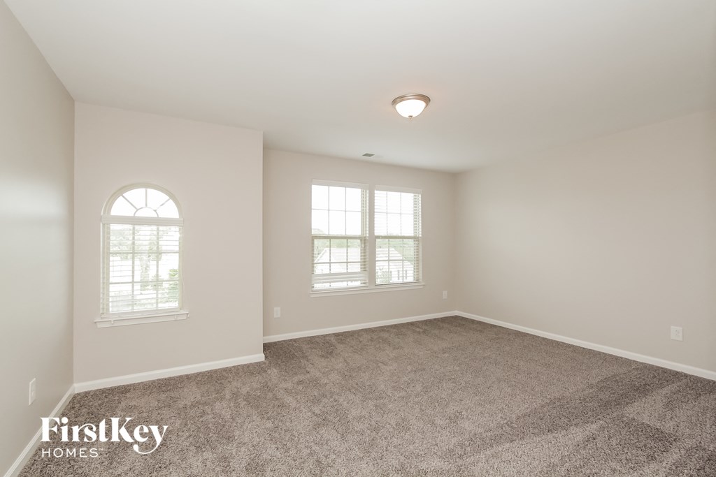 a spacious living room with carpet and two windows