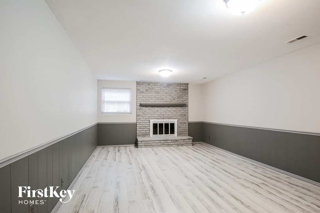 A spacious room with wooden flooring and a brick fireplace.