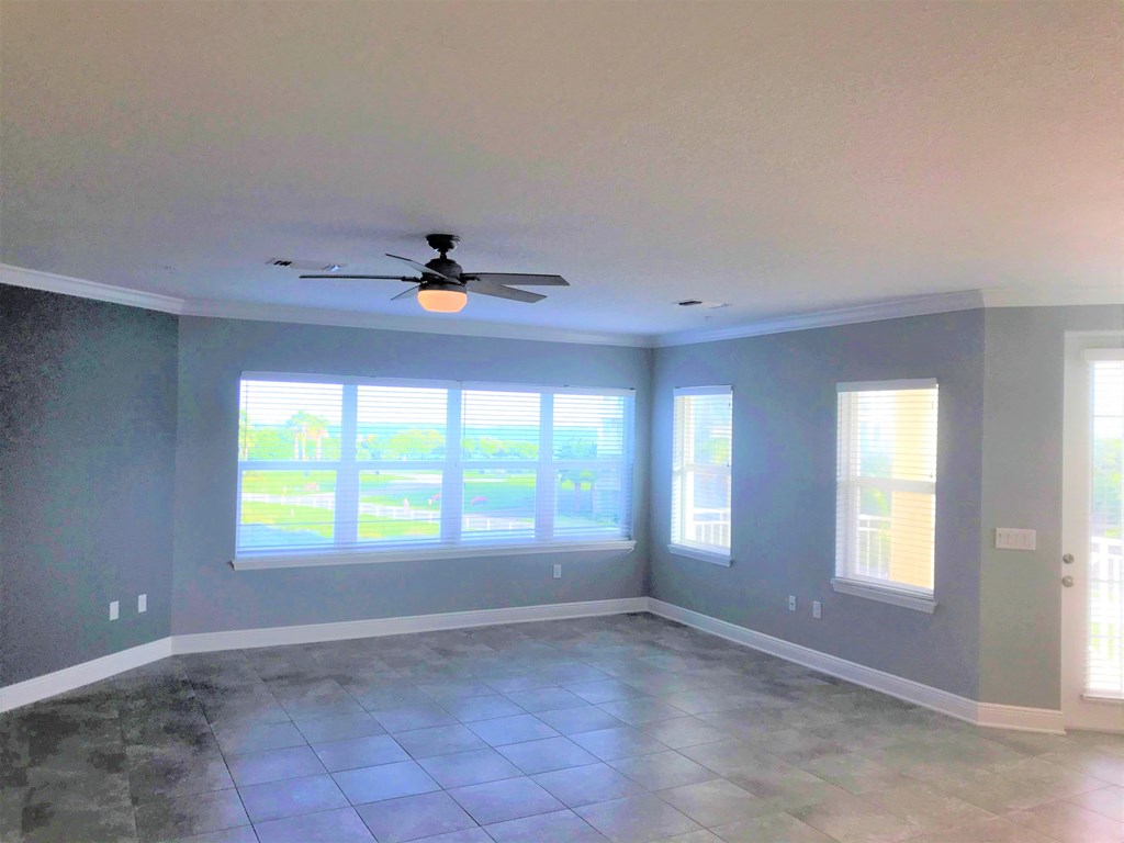 an empty living room with a ceiling fan and windows