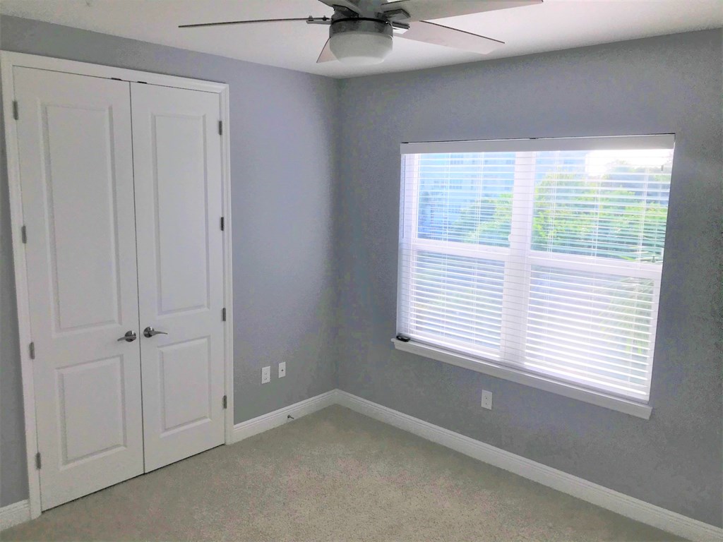 a bedroom with gray walls and a window and a ceiling fan