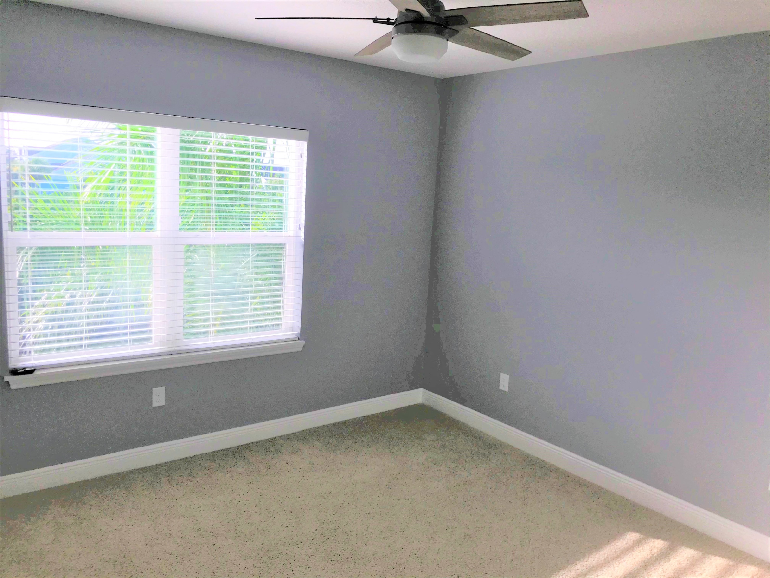 a corner of a room with a window and a ceiling fan