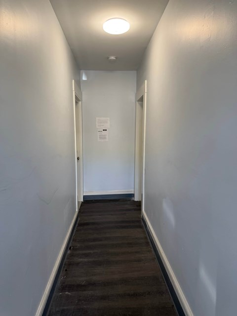 A long hallway with a white wall and a door at the end.