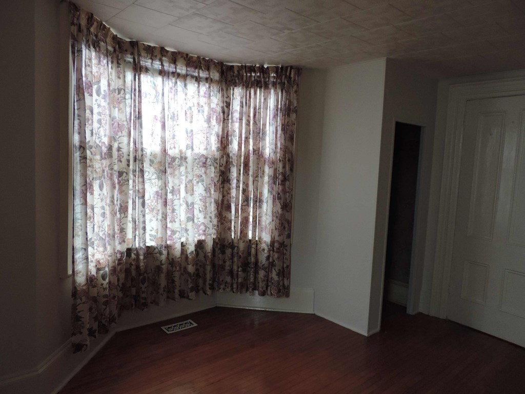 a room with a large window with curtains and a wood floor