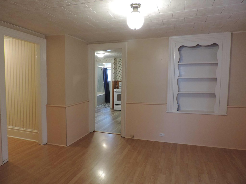 an empty living room with a wooden floor and a white wall with shelves