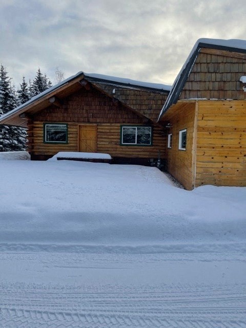 A wooden cabin sits in the snow with a cloudy sky above.