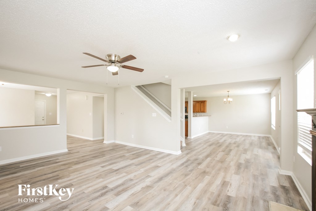 an empty living room with a ceiling fan and a kitchen