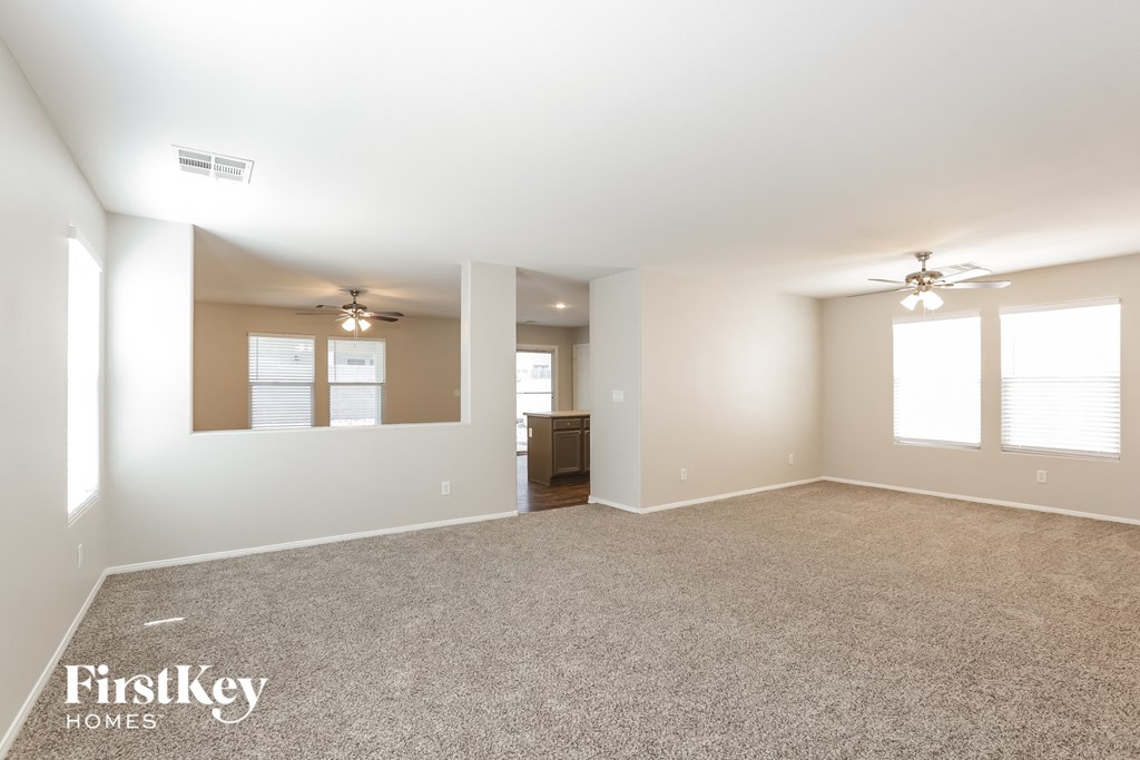 a spacious living room with carpeting and two ceiling fans