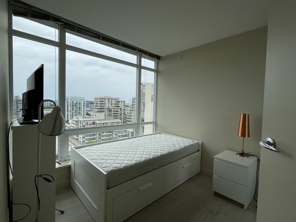A white bedroom with a large bed and a television on a stand.