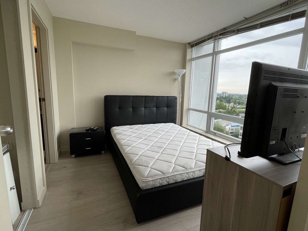 A bedroom with a large bed, a television, and a window overlooking a cityscape.