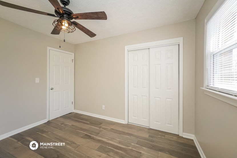 the spacious living room with two doors and a ceiling fan