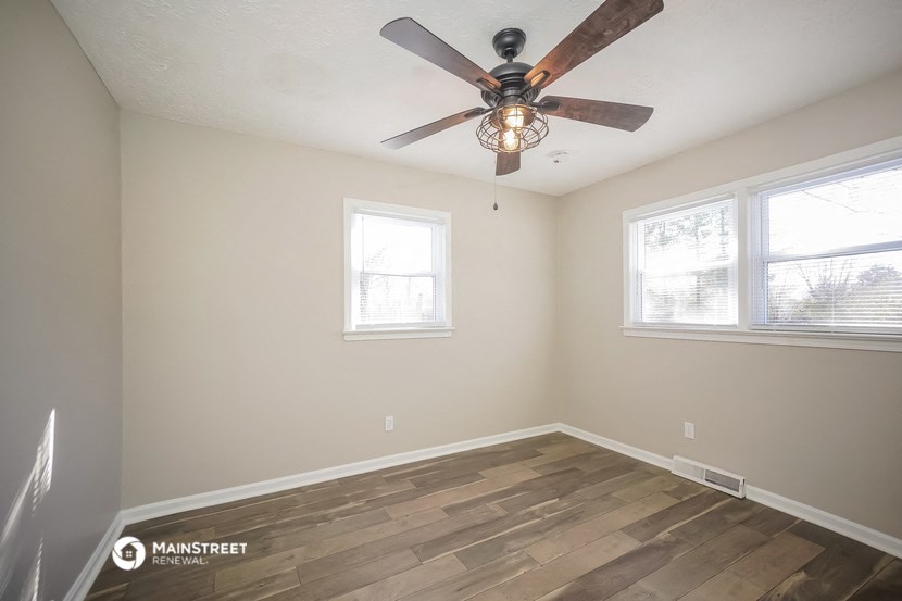 an empty room with a ceiling fan and two windows