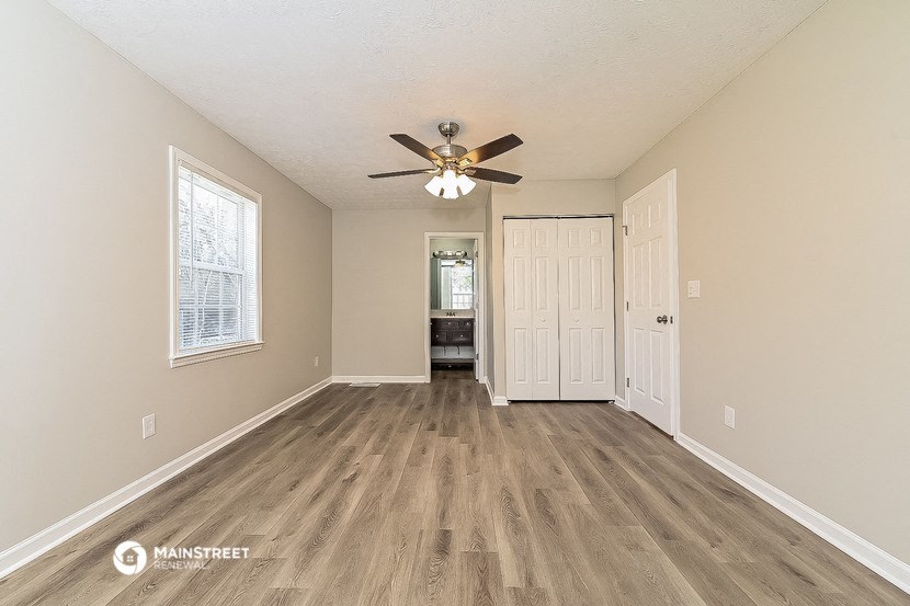 an empty living room with a ceiling fan and a door to a bedroom
