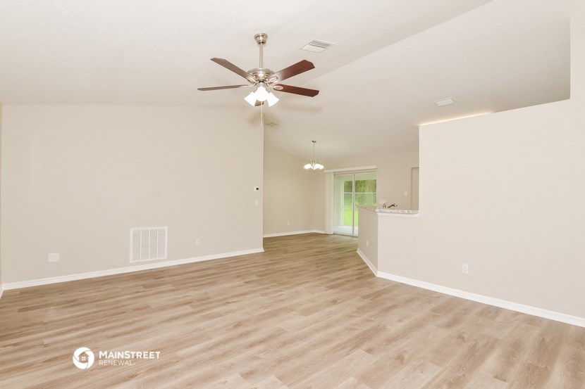 the spacious living room with hardwood floors and a ceiling fan