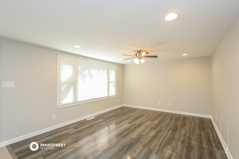 the spacious living room with hardwood floors and a ceiling fan