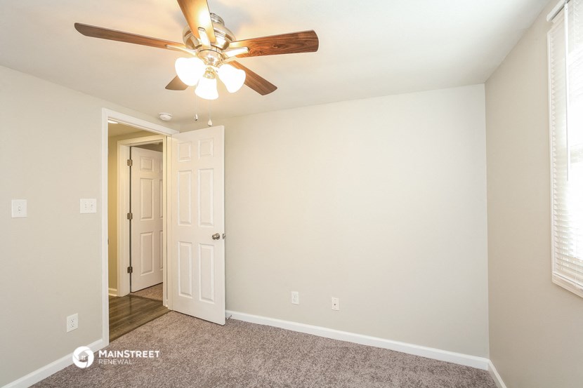the spacious living room with ceiling fan and door to the hallway