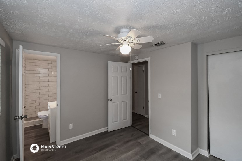 the living room of an apartment with a ceiling fan and a door to the bathroom