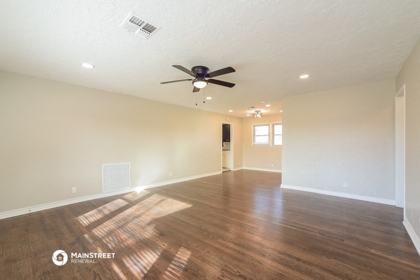 the spacious living room with hardwood flooring and a ceiling fan