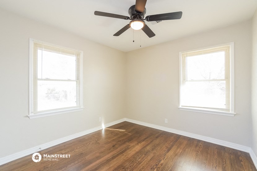 an empty room with a ceiling fan and two windows