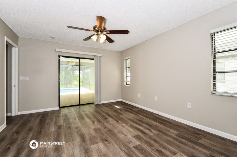 an empty living room with a ceiling fan and a door to a pool